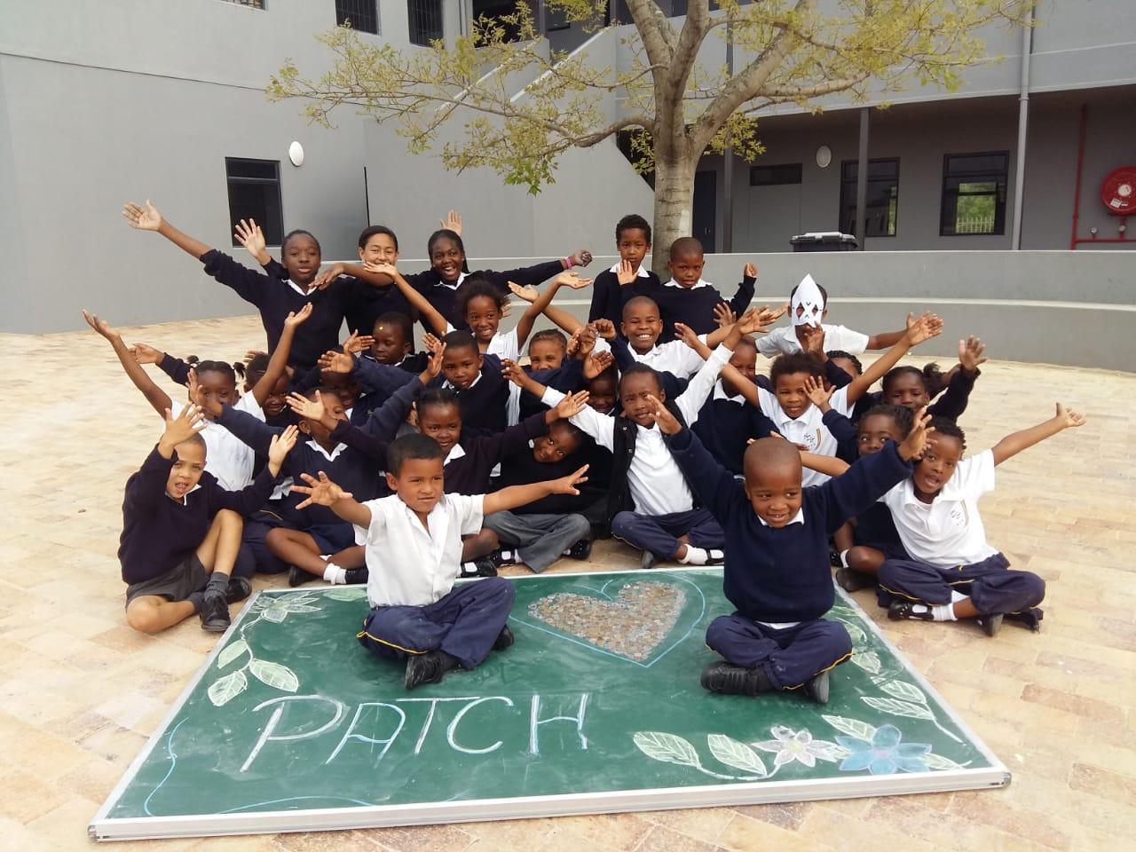 Schulkinder sitzen im Schulhof und posieren für ein Foto mit erhobenen Armen